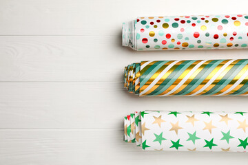 Different colorful wrapping paper rolls on white wooden table, flat lay. Space for text - obrazy, fototapety, plakaty