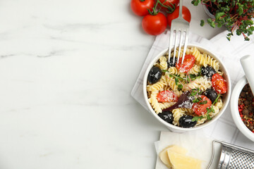 Bowl of delicious pasta with tomatoes, olives and cheese on white table, flat lay. Space for text