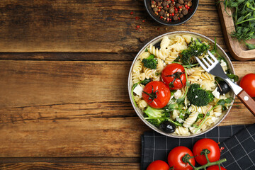 Bowl of delicious pasta with tomatoes, broccoli and cheese on wooden table, flat lay. Space for text