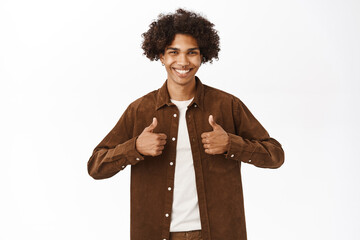 Handsome smiling young man shows thumbs up in support, pleased by smth, praise and compliment, like...