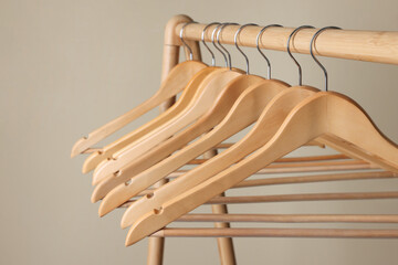 Clothes hangers on wooden rack against beige background, closeup