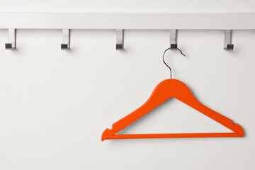 Rack with empty orange clothes hanger on white wall - Powered by Adobe