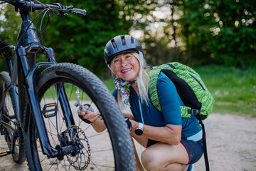 Active senior woman repairing bicycle, pumping up tire in nature in summer.
