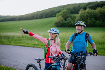 Active senior couple riding electric bicycles on road at summer park, healthy lifestyle concept.