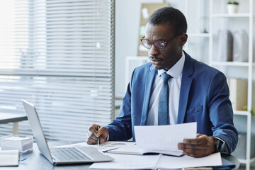 Fototapeta premium Portrait of successful black businessman wearing suit marking data report with pen in office, copy space
