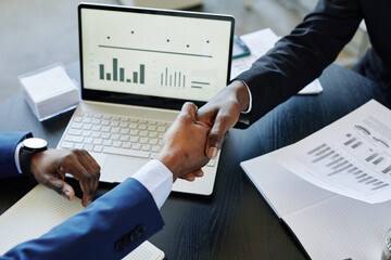 Top view close up of two impersonal business men shaking hands across meeting table in office after negotiating deal