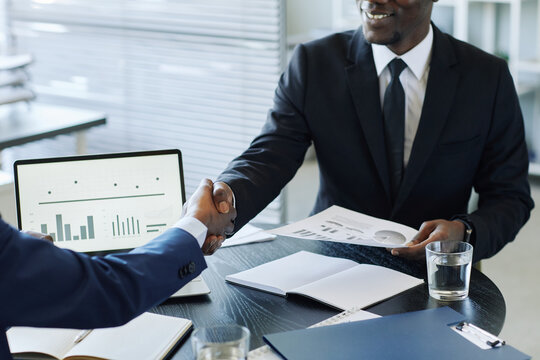 Close up of two impersonal business men shaking hands across meeting table in office after negotiating deal