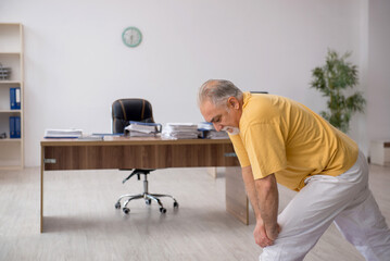 Old businessman employee doing sport exercises in the office