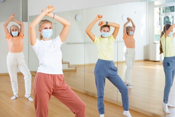 Caucasian woman in face mask learning aerobic dance with her family in studio.
