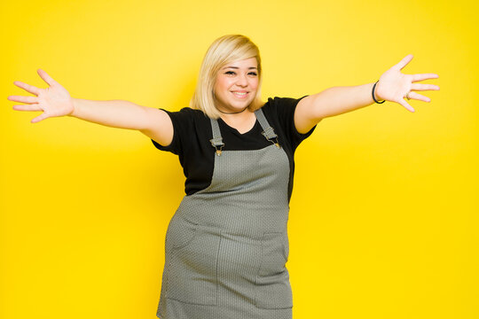Young fat woman with dyed blond hair opening her arms and giving a big hug in a studio