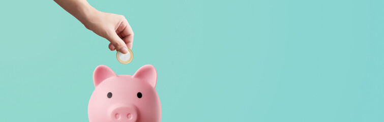 man depositing coins in a pink piggy bank on a blue background - savings concept - obrazy, fototapety, plakaty
