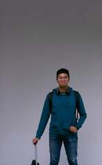 young man with suitcase in hand smiles at the camera on a neutral background with space for text