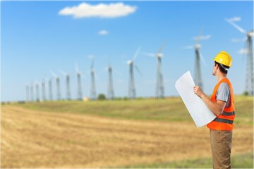 Young engineers discussing against turbines on wind turbine farm.