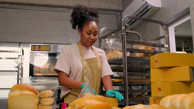 Bakery startup small business delivery. One African American female cook is packing handmade and fresh-baked bread and pastries in boxes and sending for online customer purchases in culinary kitchen.