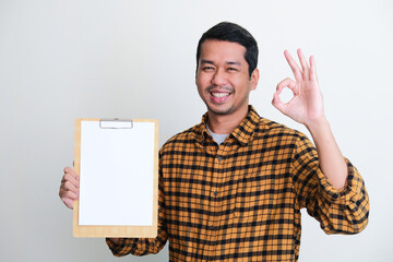 Adult Asian man smiling and give OK hand sign while showing empty white paper