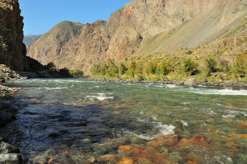 A stormy stream of a wide and beautiful river with clear water flowing along the bottom of a deep canyon.