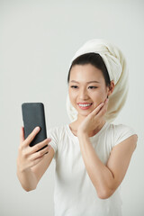 Naklejka premium Young Vietnamese woman wtih glowy skin taking selfie on smartphone after shower