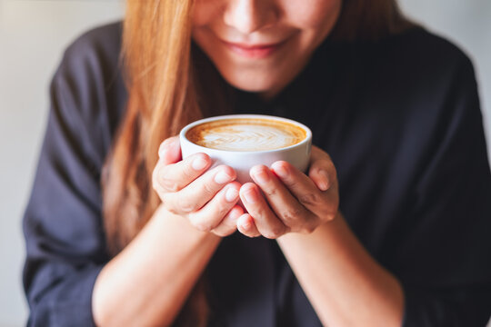 Closeup image of a young asian woman holding and drinking hot latte coffee