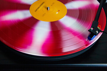 Red, Pink and white vinyl record spinning on a turntable, stylus on the record, blurred motion, in...