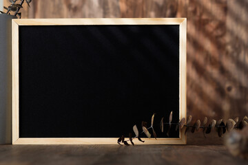 blank blackboard frame with kitchenware on wood table with sunlight