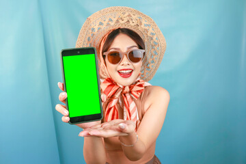 Fototapeta na wymiar Traveling concept of a young Asian happy woman showing copy space on her smartphone isolated by a blue background
