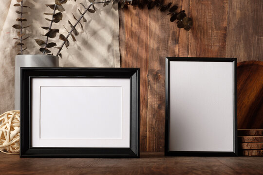 blank black photo frame with kitchenware on wood table with sunlight