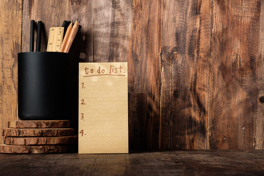 brown note paper to do list on wood wall and pencil box with sunlight