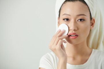 Portrait of young woman applying face toner with cotton pad to restore skin pH level