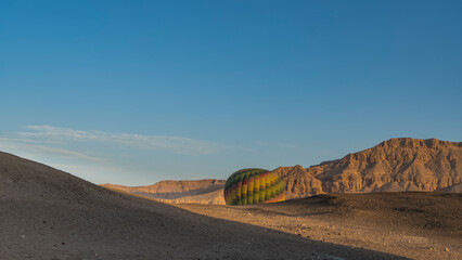 A bright balloon rises from the gorge above the desert plateau.  Shadows on the sand. A picturesque...