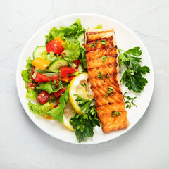 Salmon steak with vegetables and fries on light background.