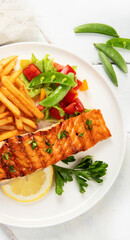Salmon steak with vegetables and fries on light background.