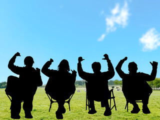 キャンプ場でアウトドアチェアに座って両手を上げる男女4人のシルエット