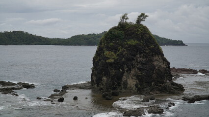 Coral rock on the beach and hit by the wave with cloudy sky.  Watu Lumbung Beach, Yogyakarta,...