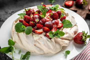 Homemade delicious meringue cake Pavlova with whipped cream, fresh strawberries and mint on wooden background, place for text, top view