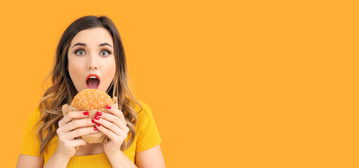 Portrait of beautiful surprised young woman with burger on orange background with space for text