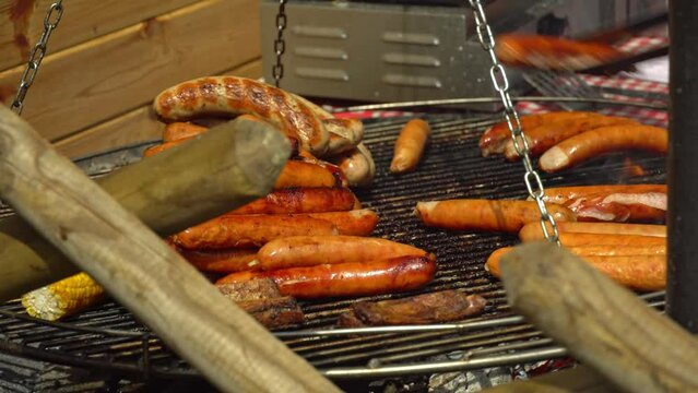 Chef flips sausages Bratwurst roasting with cooking tongs. Street food for picnic and camping. BBQ grilling frankfurt beef sausage. Grilled weisswurst fried and smoked in charcoal grills. 4k footage