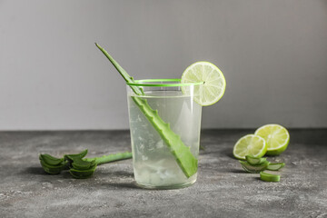 Glass of aloe juice with leaf and lime on table against grey background
