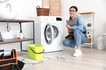 Obraz premium Asian female plumber with clipboard near washing machine in bathroom