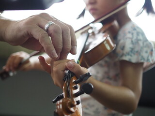 Close up hands of little girl and teacher on violin lesson in the room.