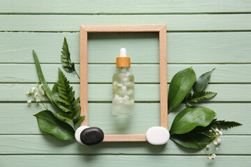Composition with bottle of serum, empty picture frame and plant leaves on color wooden background