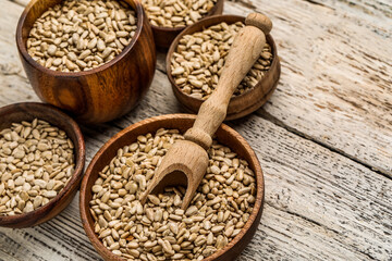 Bowls with peeled sunflower seeds and scoop on white wooden background, closeup