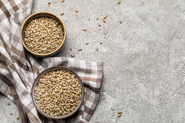 Bowls with peeled sunflower seeds and napkin on light background