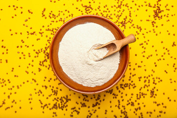Bowl of flour with scoop and buckwheat grains on yellow background