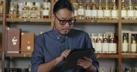 A young Asian sommelier is checking the drink store. A bartender wearing glasses and a hair tie Wine stands to check the drink list and prepares to serve drinks to customers at the hotel bar.