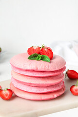 Board with tasty pink pancakes and strawberry on table, closeup