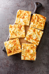 Alevropita is a feta pie made with a flour-based batter which originates from north-western Greece close-up on a wooden board on the table. Vertical top view from above