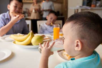 Little boy drinking glass of milk at breakfast table
