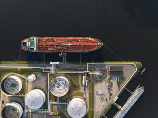 Petrochemical energy heavy transport industry cargo vessel tanker top down aerial drone view. Docked bulk carrier ship along storage facility silos. Energy gas and lpg petroleum commercial industry. © Sepia100