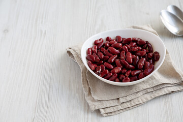 Obraz na płótnie Canvas Red Organic Kidney Beans in a White Bowl on a white wooden background, side view. Copy space.