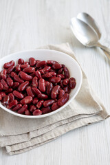 Red Organic Kidney Beans in a White Bowl on a white wooden background, side view.